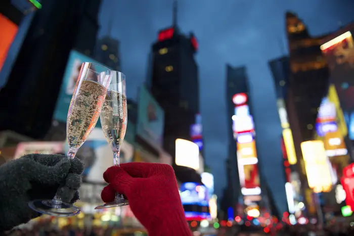 Two champagne glasses held up in a toast in a brightly lit Times Square NYC.